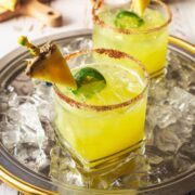 Two pineapple mocktails on a tray with ice.