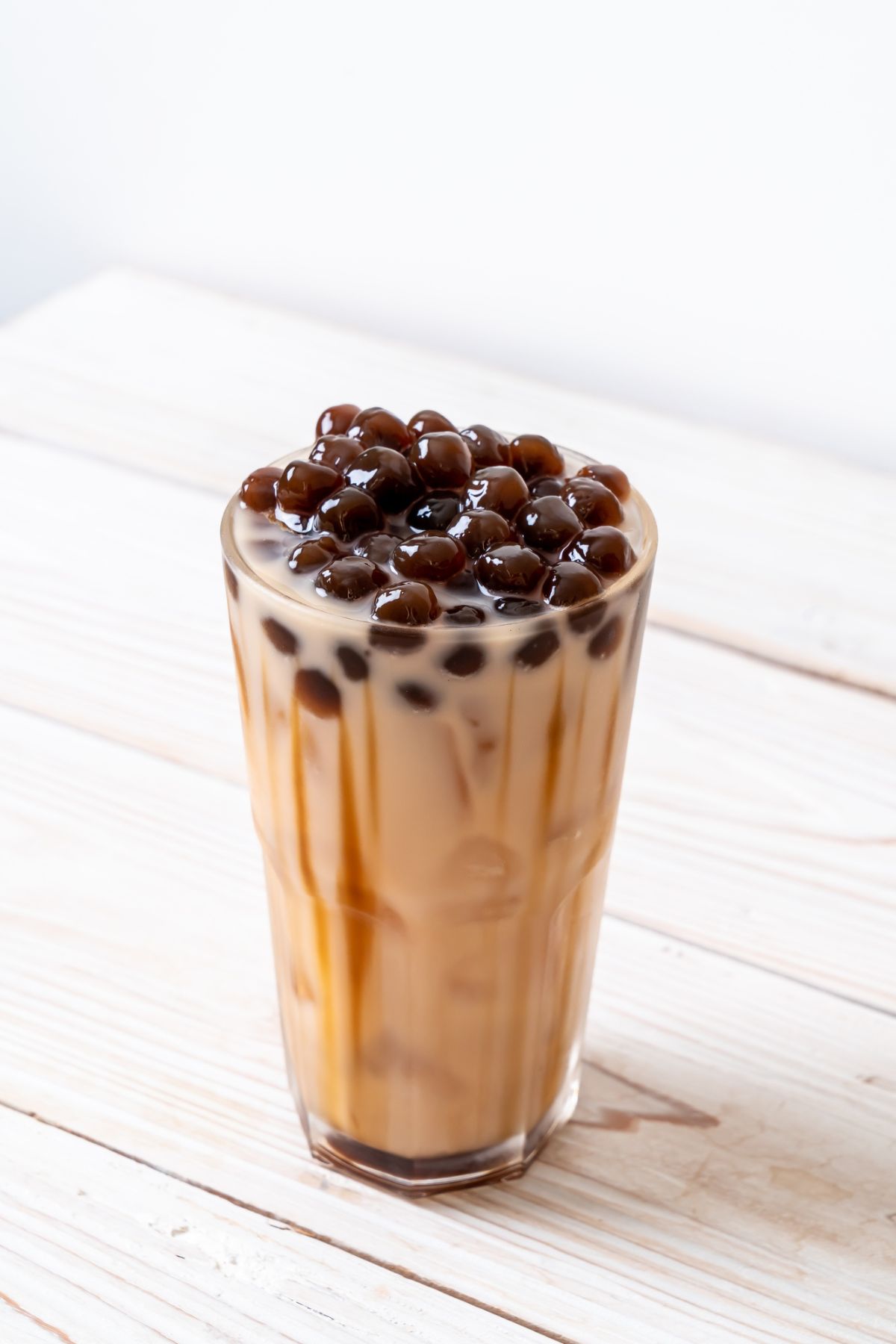 A glass of iced boba tea with layers of tea, milk, and a generous amount of dark tapioca pearls on top.