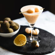 A Virgin Lychee Mojito mocktail is sitting on a table next to a bowl of fruit.