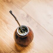 A traditional mate cup with a metal straw, known as a bombilla, filled with yerba mate for making at home, placed on a wooden floor.